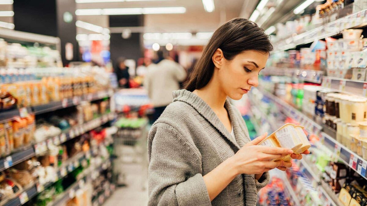 Eine Frau sieht sich in einem Supermarkt ein Produkt genauer an und liest die Produktbeschreibung.