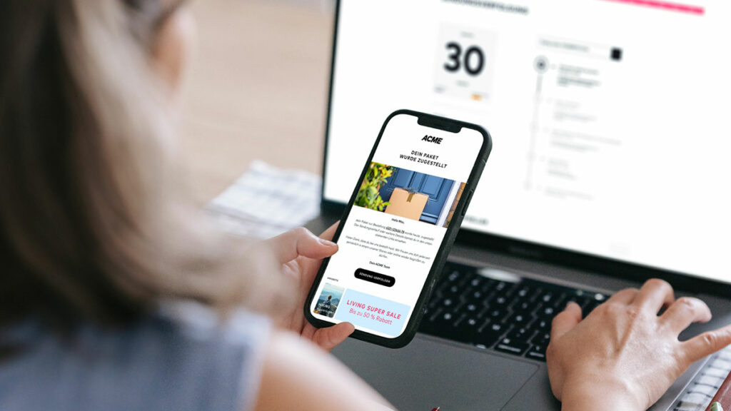 Eine Frau erhält auf ihrem Smartphone eine Benachrichtigung, dass ihr Paket zugestellt wurde. Parallel ist auf ihrem Laptop die zugehörige Track & Trace-Seite geöffnet.